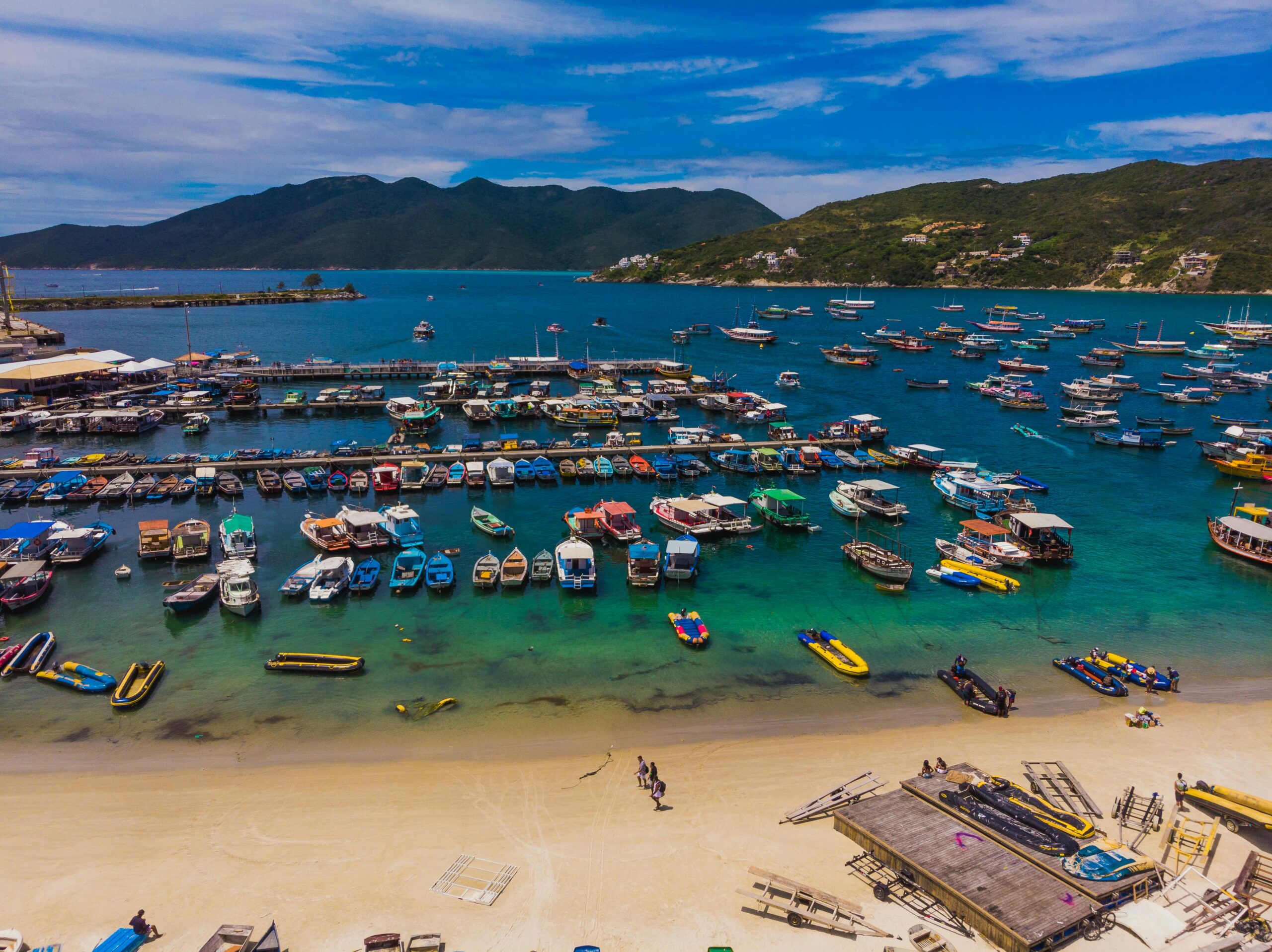 Colorful boats docked at Arraial do Cabo's stunning beachside with clear blue water and mountains in the background.